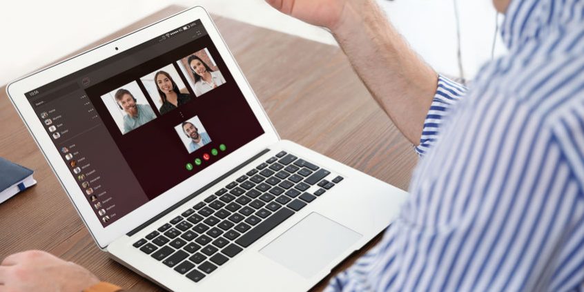 Man having video chat with colleagues at table in office, closeup