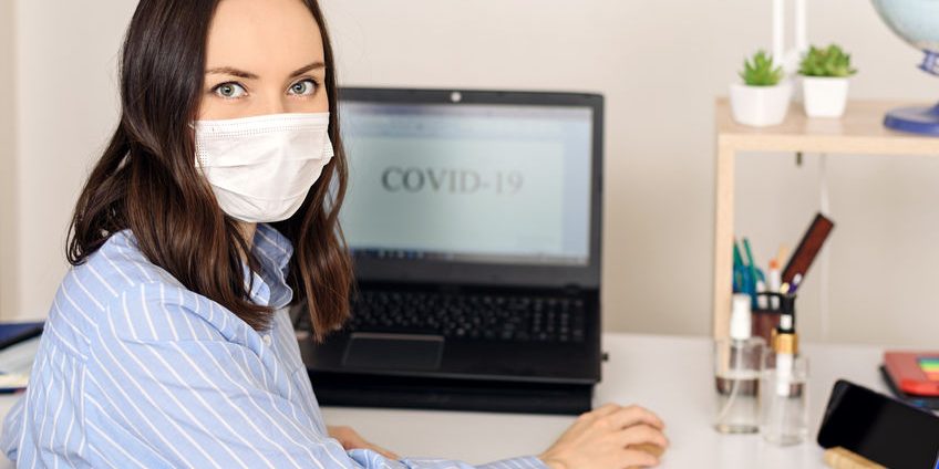 woman in medical mask wrote word covid-19 on monitor screen, remote work at home, coronavirus, pandemic