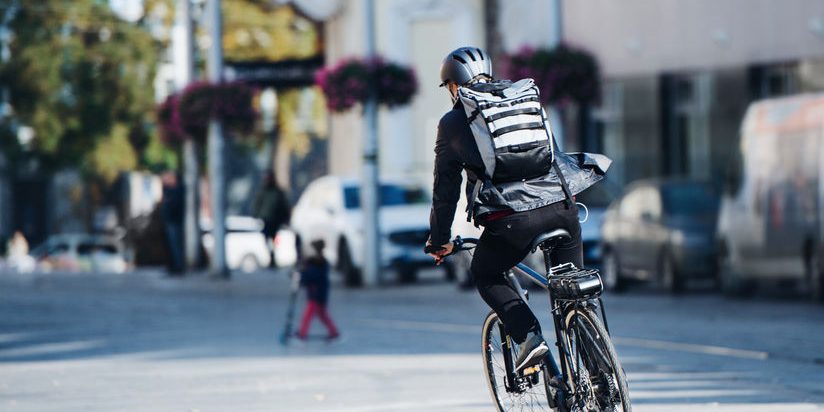 A rear view of male bicycle courier delivering packages in city. Copy space.