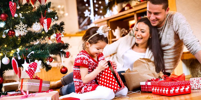 Young family with daughter at Christmas tree at home.