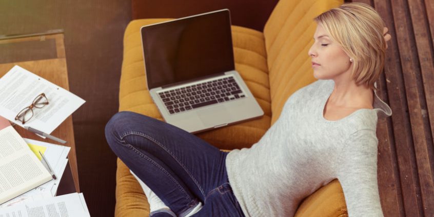 Tired Woman Leaning on Sofa with Laptop and Papers
