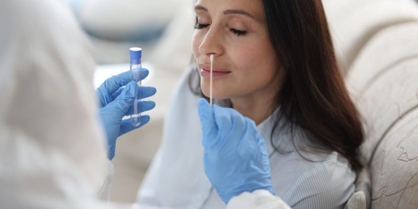 Doctor laboratory assistant in protective suit takes swab from nose of sick patient at home