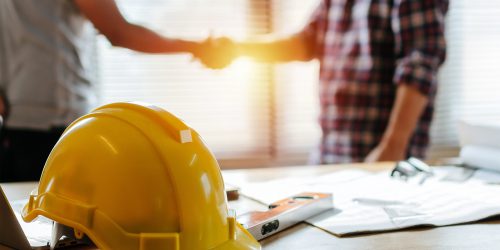 Yellow,Safety,Helmet,On,Workplace,Desk,With,Construction,Worker,Team