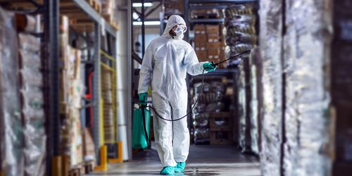 Man,In,Protective,Suit,And,Mask,Disinfecting,Warehouse,Full,Of